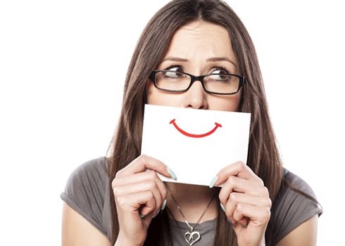 A woman holding up a card with a drawn on happy face in front of her mouth