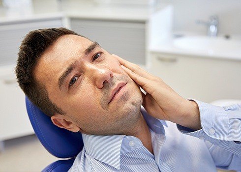 Man in dental chair hilding cheek